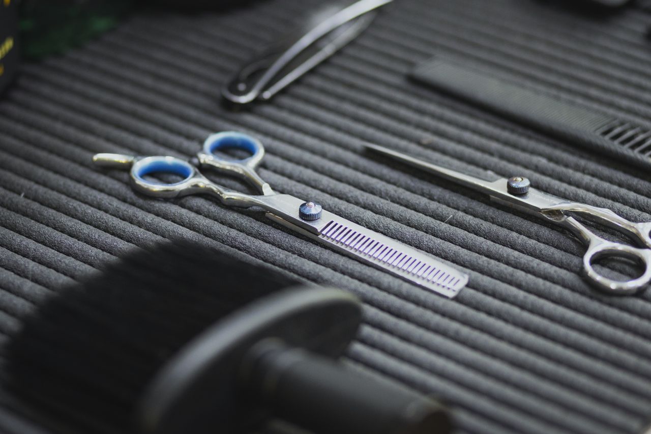 Close-up of hairdressing scissors and combs on a textured surface for salon use.